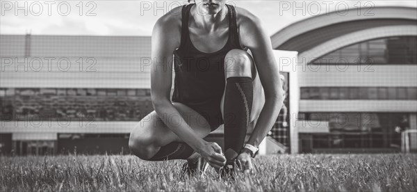 Portrait of a young runner who laces her boots at a football stadium. Sports concept.
