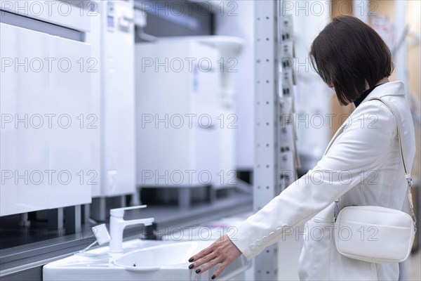 Beautiful young woman in a white jacket chooses plumbing supplies in a hardware store