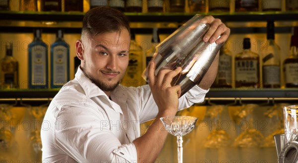 Charming bartender prepares cocktails in two shakers.