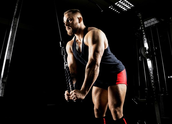 The athlete performs an exercise on the triceps on a special device. Side view