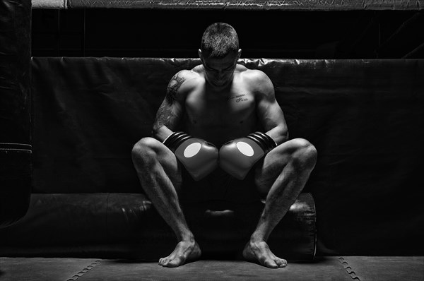 Boxer sits in gloves near the ring with his head bowed. The concept of sports