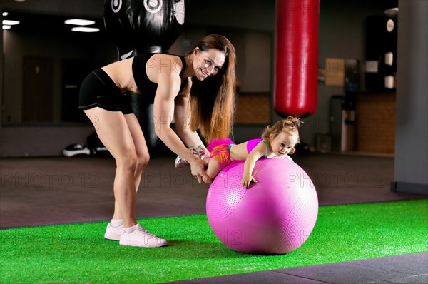 Mom is engaged with her daughter in the gym with a fitness ball.