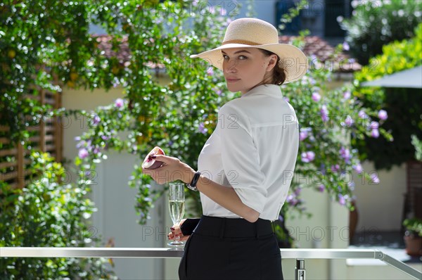 Charming girl is standing in the garden with a glass of champagne and a peach. The concept of vacation