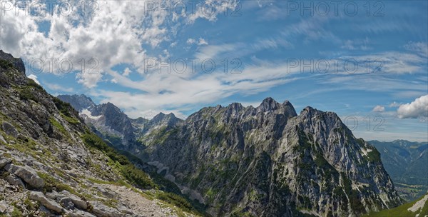 Panorama of an impressive mountain range with snow-covered peaks under a blue sky with clouds