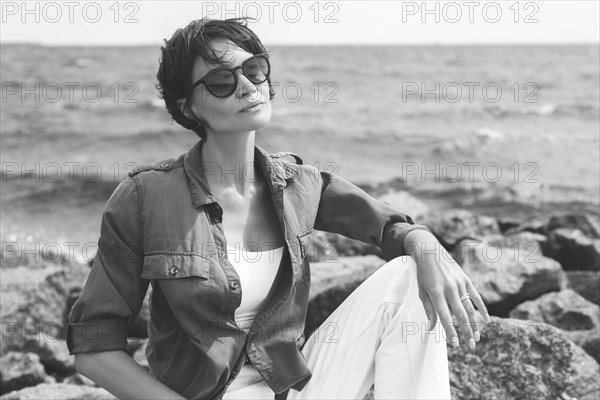 Portrait of a stylish woman sitting on stones in the bay. Windy weather. Happiness