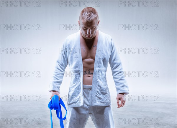 Athlete in a kimono with a blue belt stands with his head down. The concept of karate and judo.