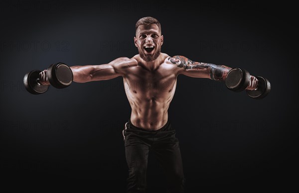 Handsome young man spreads his arms with dumbbells to the sides. Shoulder pumping. Fitness and bodybuilding concept.