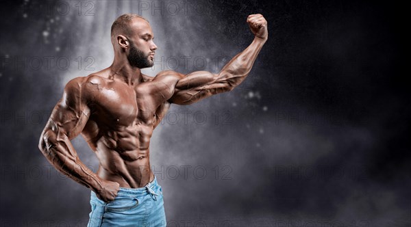 Isolated athlete on a background of smoke with small dust particles. Bodybuilding concept.