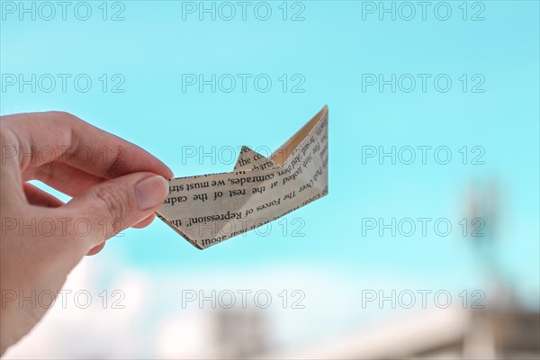 Hands holding an origami paper boat up against a clear blue sky background