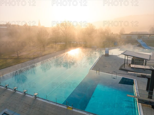 Morning light reflected in the water of a fog-covered swimming pool with slides