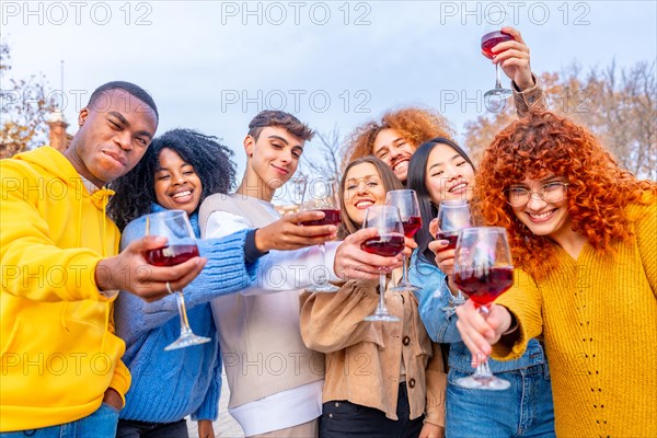 Multi-ethnic friends toasting with red wine smiling at camera together in the street