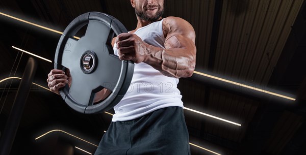 Portrait of a man in a white T-shirt exercising in the gym with barbell discs. Biceps pumping. Fitness and bodybuilding concept.