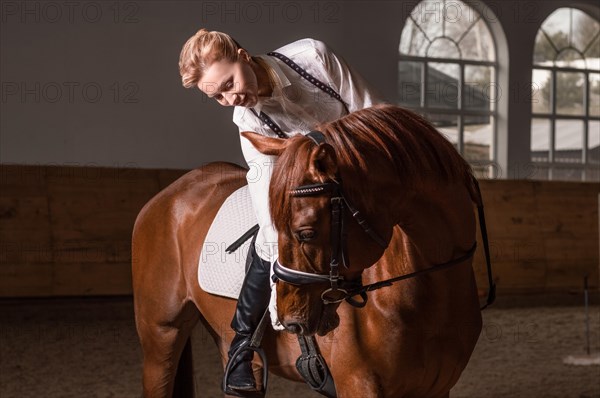 Image of a woman riding a thoroughbred horse. The background is a racing arena.