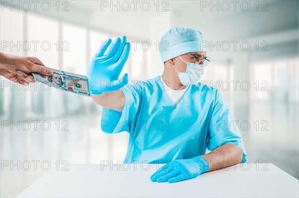 The doctor sits at his desk and refuses a bundle of hundred-dollar bills. Honest medicine concept.