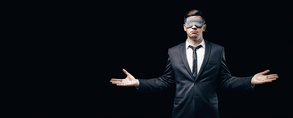 Portrait of a man in a mask for sleeping. He stands against a black wall. Blind business concept. Work during the crisis.