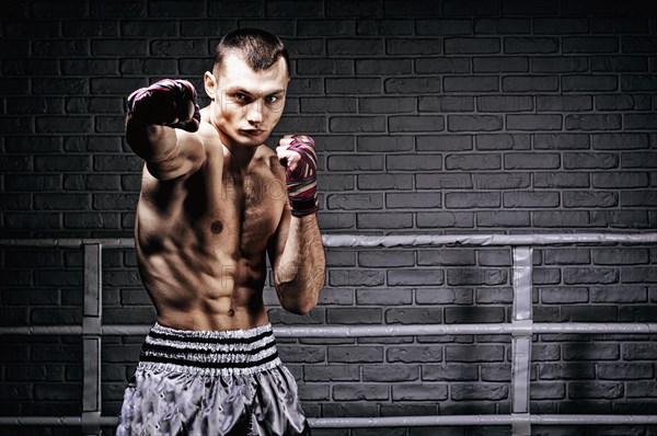 Thai boxer stands in the ring and punches in front of him. The concept of sports