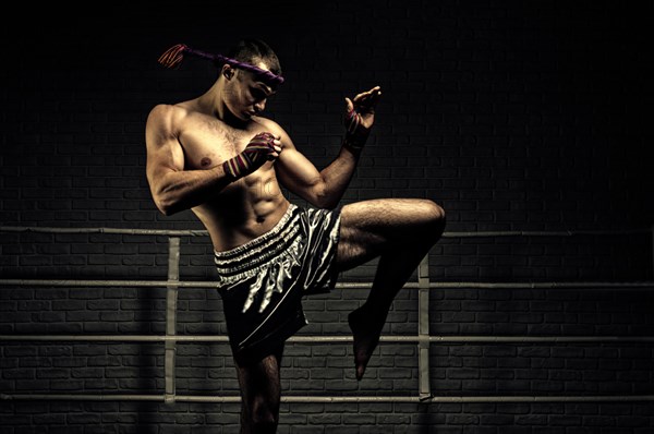 Kickboxer in the ring surrounded by searchlights stretches before the fight. Makes swing movements with his knee. Mongkhon.