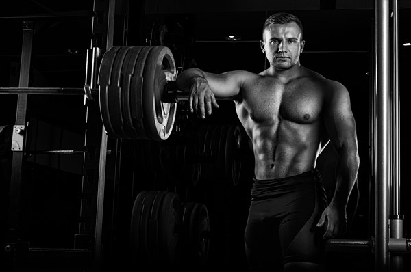 The weightlifter leans his hand on the barbell and looks menacingly forward. Front view