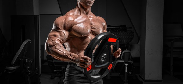 Muscular man posing in the gym with a barbell disc. Bodybuilding and powerlifting concept.
