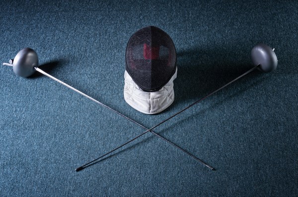 Two swords and mask lie on a blue background. The concept of fencing.