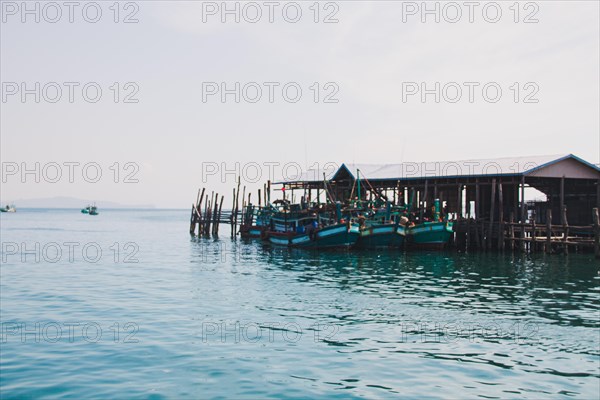 Fishing boats moored at a wooden pier in a serene waterfront village. Koh Sdach Island