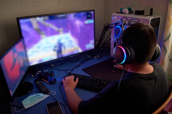 Back view of teenage gamer boy playing video games online on computer in dark room