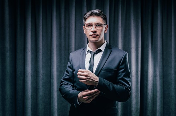 Adult man is standing in a suit against a black curtain. Business concept. The administrative staff of the company.