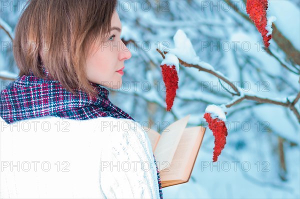 Portrait of a charming girl who reads a book in the winter forest. Concept of Christmas