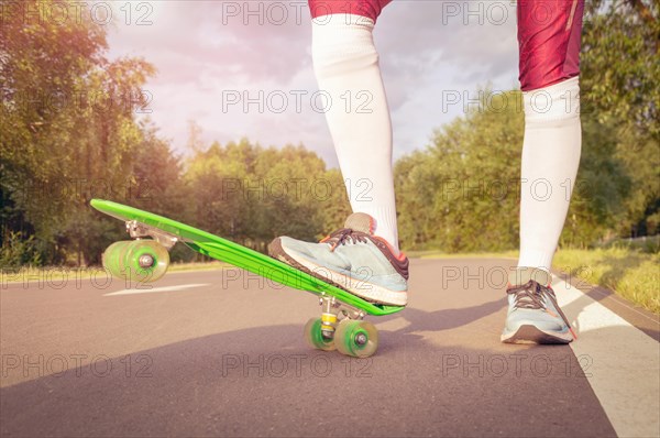 Images of a leg standing on a skateboard. Sunny evening in the park. Skateboarding concept.