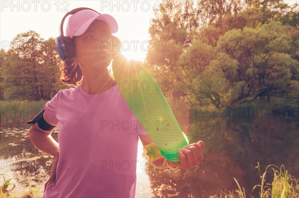 Image of a woman in a cap and headphones with a skateboard. Sunset in the park. Vacation concept.