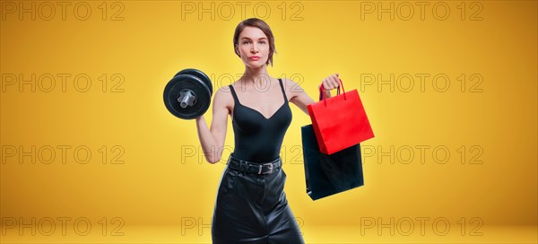 Beautiful slender woman posing in the studio with a dumbbell and gift bags. Gift concept. Gym membership