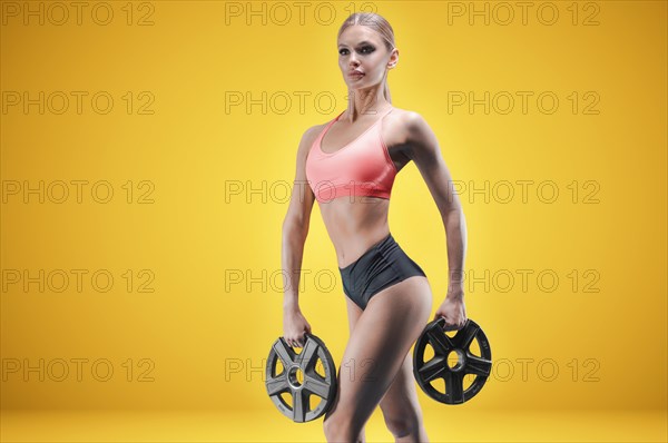 Portrait of a tall athletic woman with weight plates in her hands. The concept of sports