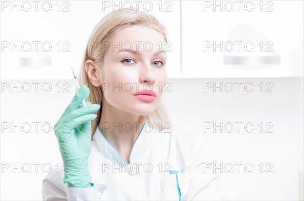 Portrait of a blonde girl in a medical gown with a syringe in her hands. Medical center advertisement.