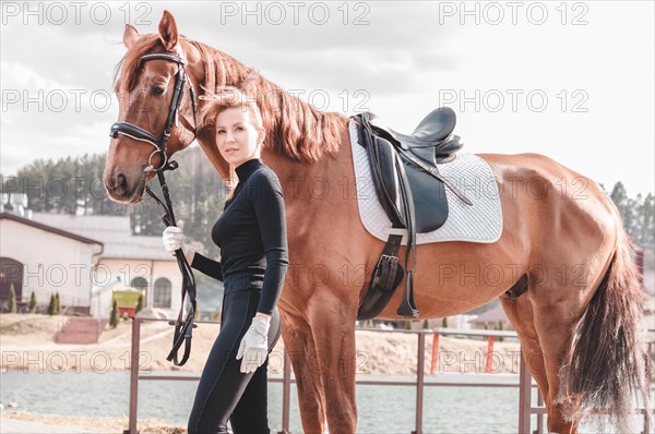 Beautiful stylish woman walking with a horse in a country club. Equestrian sport