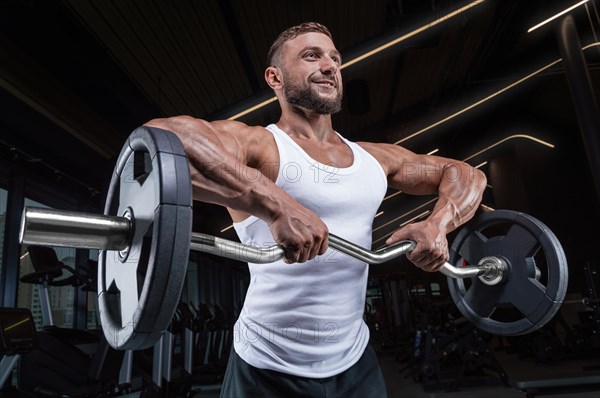 Handsome young man working out with a barbell in the gym. Shoulder pumping. Barbell pull to the chin. Fitness and bodybuilding concept