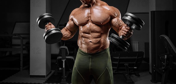 Powerful bodybuilder works out in a gym with dumbbells. No name portrait. Bodybuilding concept.