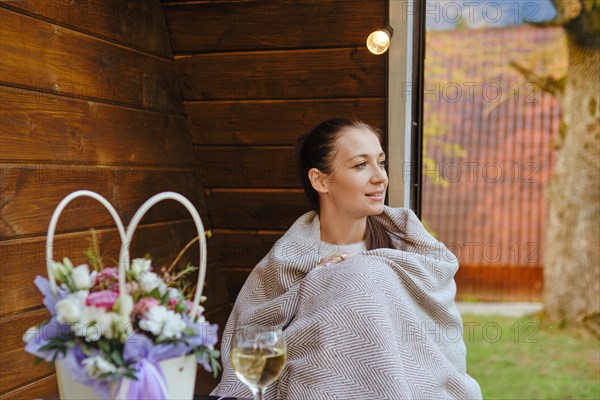 Woman wrapped in plaid sitting on veranda looks away with interest