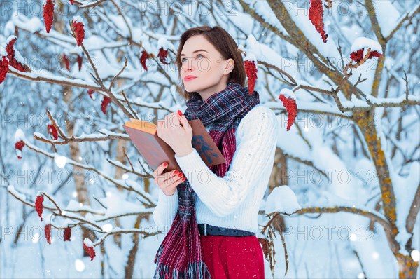 Portrait of a charming girl who reads a book in the winter forest. Concept of Christmas