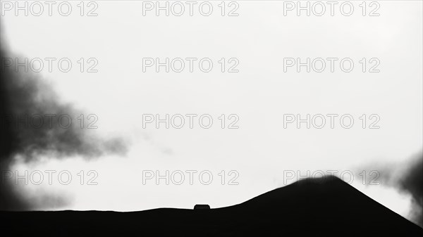 Grassy mountain peak with mountain hut in the fog