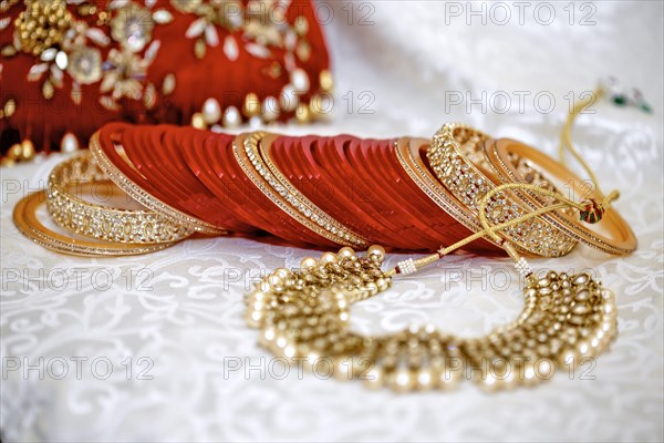 Elegant traditional Indian wedding jewelry with red bangles and gold accents on an embroidered fabric