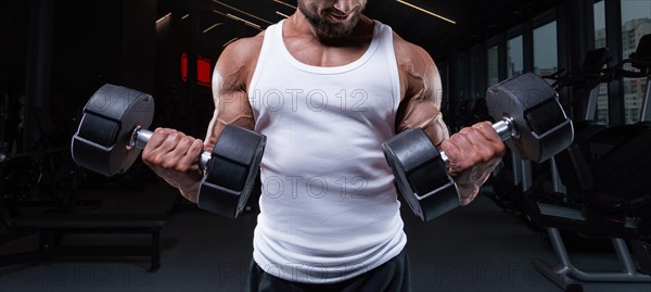 Portrait of a man in a white T-shirt exercising in the gym with dumbbells. Biceps pumping. Fitness and bodybuilding concept.