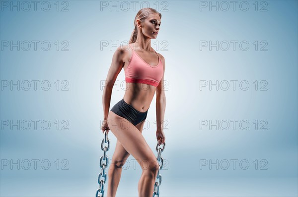 Charming tall sportswoman posing in the studio on a blue background with chains in her hands. The concept of sports
