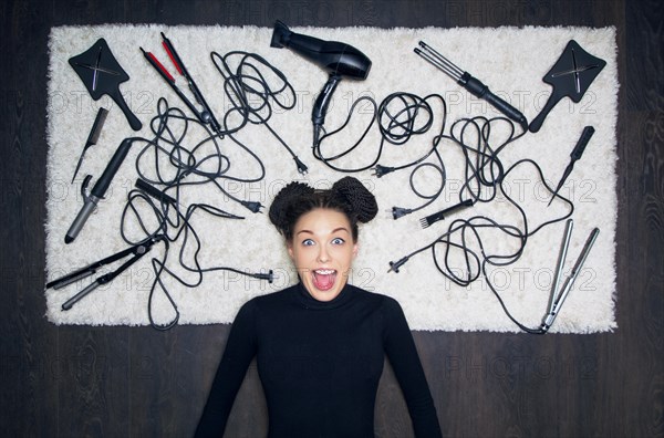 Young charming girl with dreadlocks on her head is shouting in surprise. The girl is lying on a white carpet. Around the tools for creating a haircut