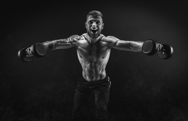 Handsome young man spreads his arms with dumbbells to the sides. Shoulder pumping. Fitness and bodybuilding concept.