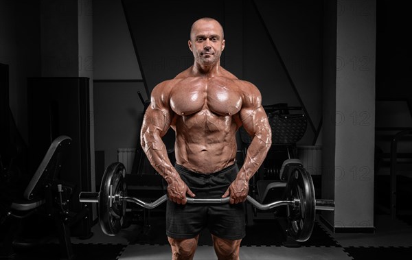 Professional weightlifter posing in the gym with a barbell in his hands. Classic bodybuilding.