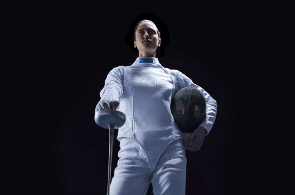 Charming girl dressed as a fencer posing with a mask and a sword. The concept of fencing.