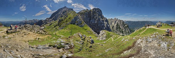 Panoramic view of a mountain landscape with hikers and green slopes under a blue sky