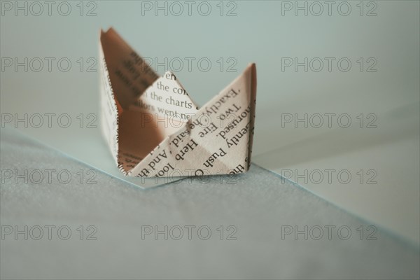 A sepia-toned origami paper boat with soft shadows on a light surface