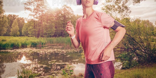 Portrait of a beautiful girl running in a sunny park in headphones with a smartphone. Music apps concept.