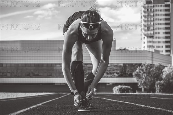 Image of a young female runner laces her shoes on a stadium track. Sports concept.